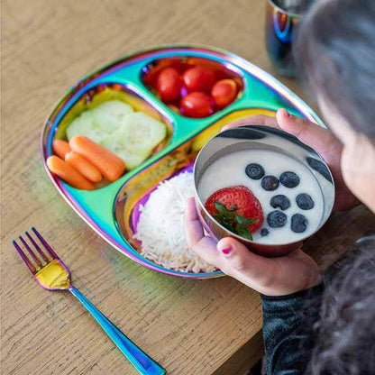 Child enjoying healthy meal on stainless steel rainbow plate with fruits, vegetables, rice, and colorful fork.